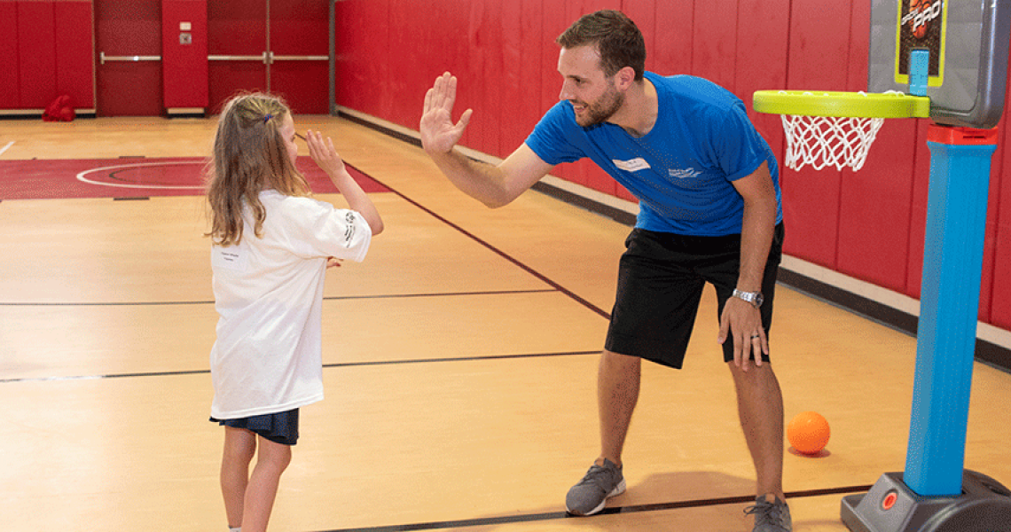 Adult high-fiving a child on a basketball court