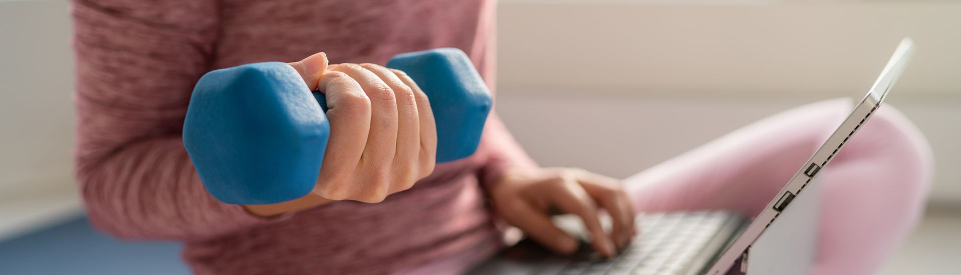 Close-up of hand holding a dumbell weight and the other hand on a laptop